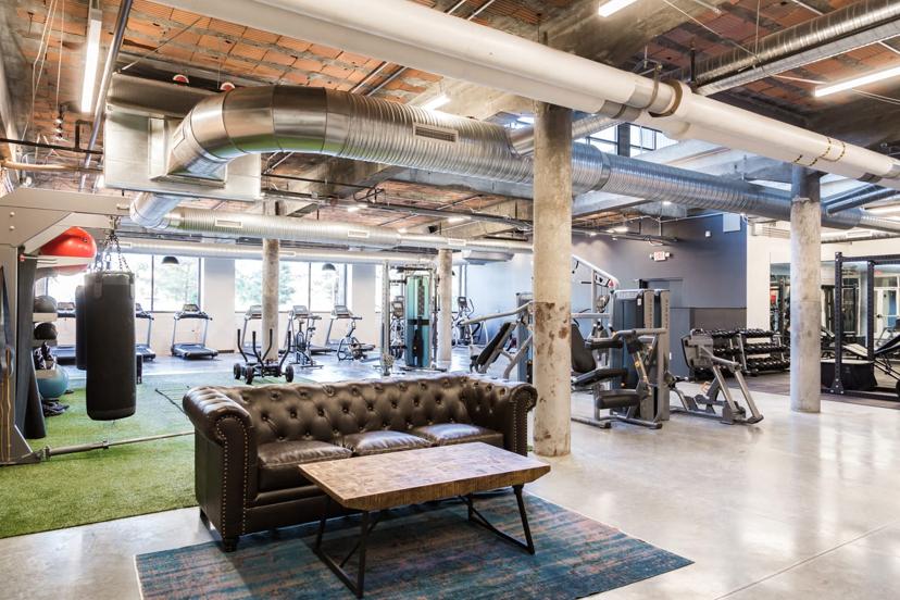 Modern gym interior with fitness equipment, a punching bag, treadmills, and free weights. A leather sofa and table are in the foreground.