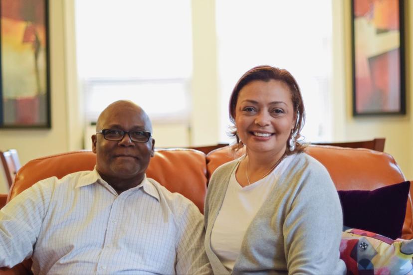 Smiling couple seated on a sofa in a warmly lit room with colorful artwork on the walls.