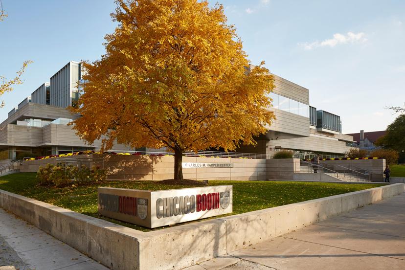 Modern building with large glass windows, surrounded by a lush garden and an autumn tree with golden leaves. Chicago Booth sign in the foreground.