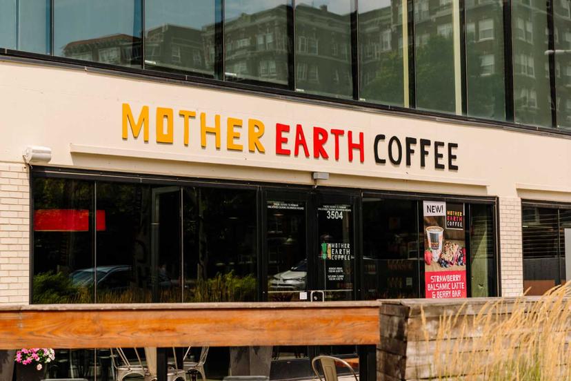 Front exterior of Mother Earth Coffee shop with large logo above entrance and poster advertising a strawberry balsamic latte and berry bar.
